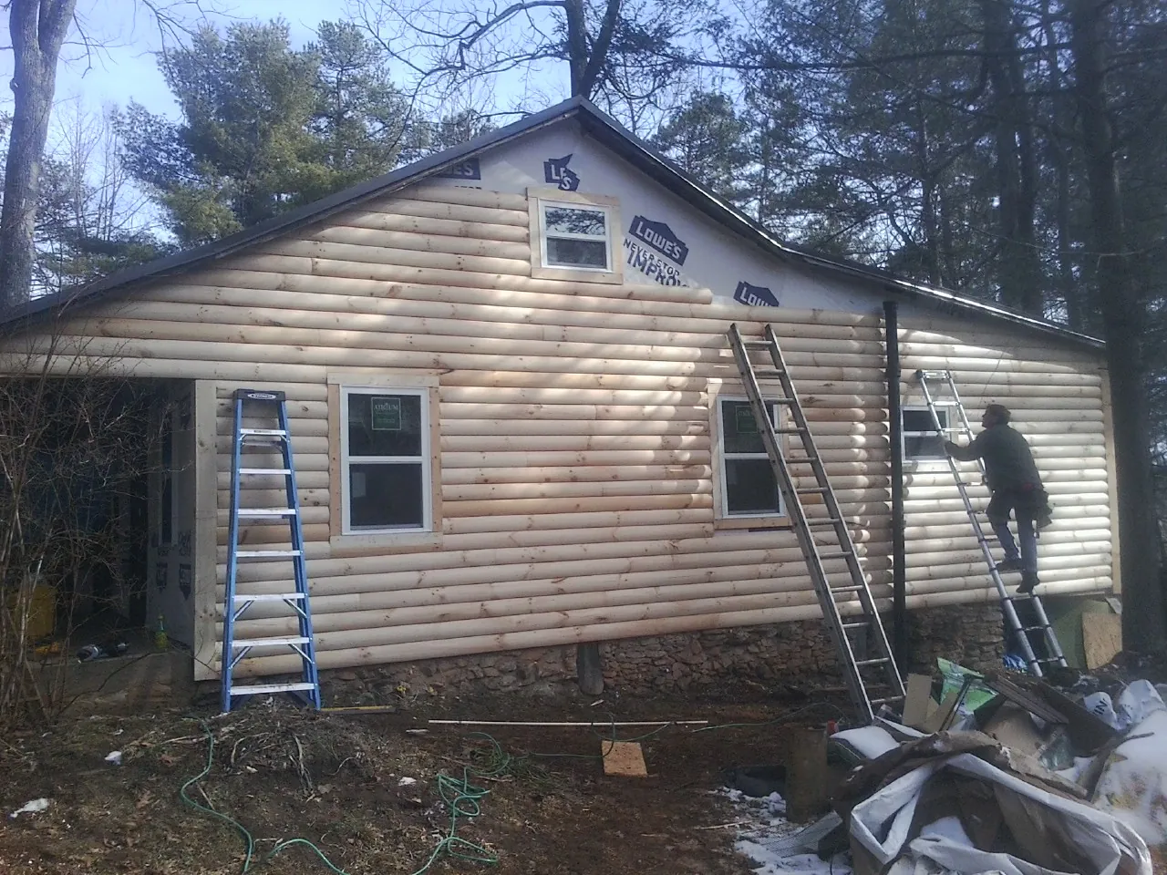 Ladders set against fresh log siding during an exterior remodel in Rochester